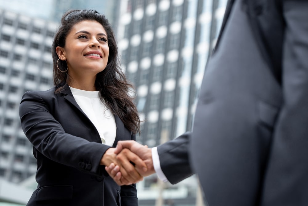 Young smiling Hispanic real estate businesswoman making handshake with partner in the city for greeting, dealing, merger and acquisition concepts