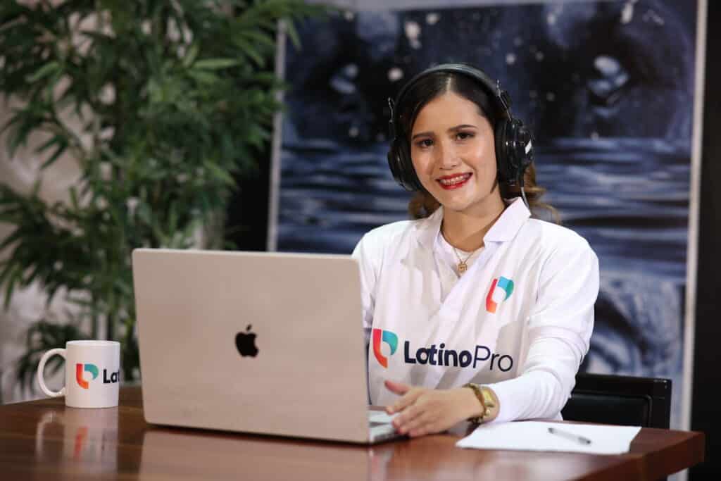A smiling woman  looks at the camera, seated at a desk with a laptop, showcasing efficient operations assistant work.