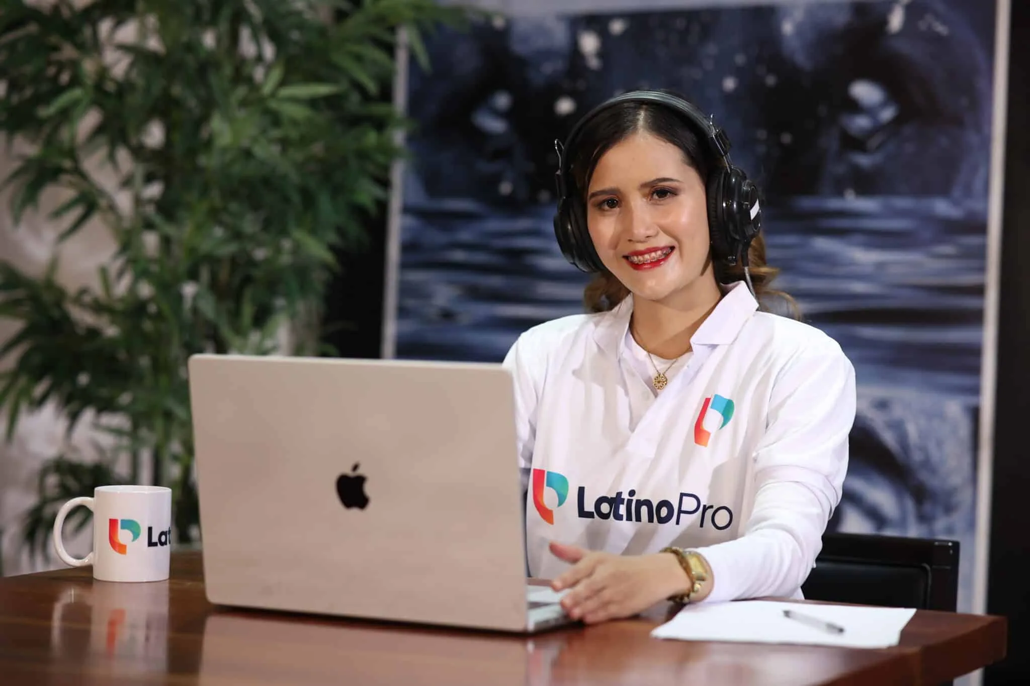 A smiling woman  looks at the camera, seated at a desk with a laptop, showcasing efficient operations assistant work.