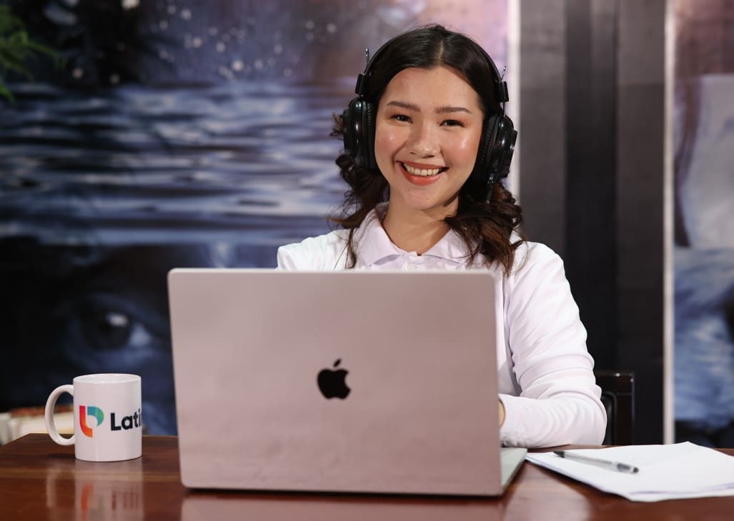 A smiling woman wearing headphones, working on her laptop as a remote receptionist