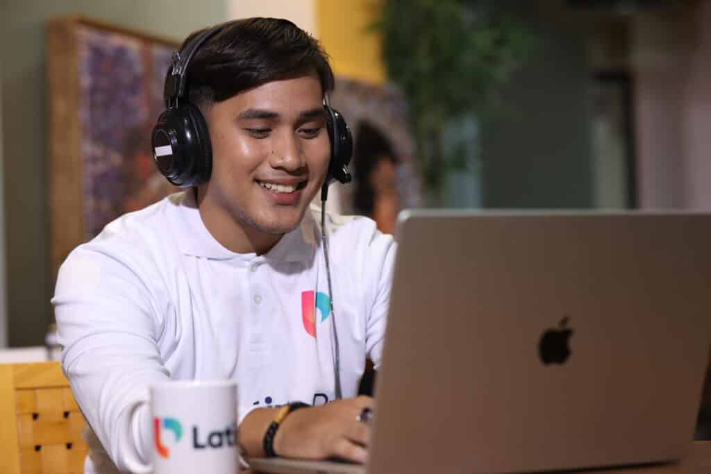 Man with headphones smiling while working on laptop, representing efficient operations assistant work.