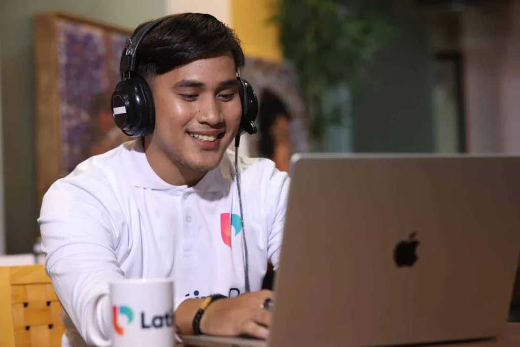 Man with headphones smiling while working on laptop, representing efficient operations assistant work.