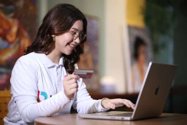 Smiling woman shops online with laptop and card, reflecting the ease of earning an accounting virtual assistant salary.