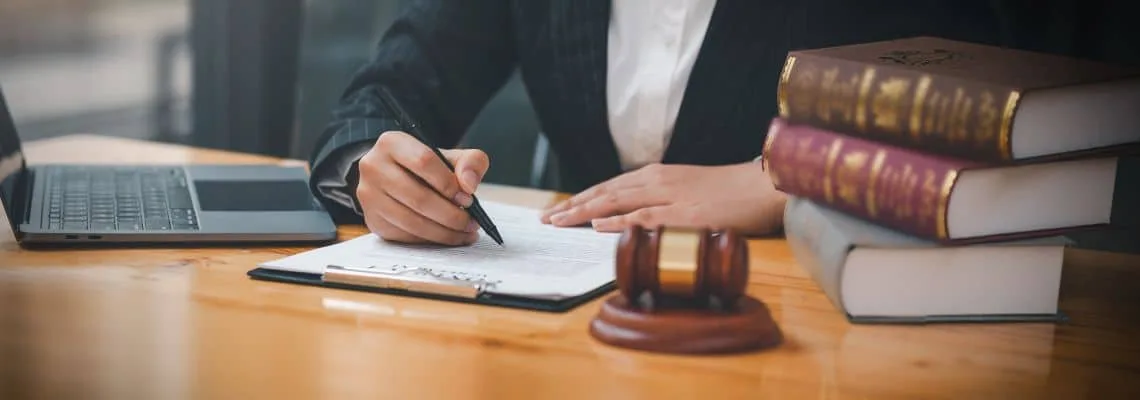 A professional signs legal documents with a laptop and gavel nearby, representing paralegal assistant jobs.