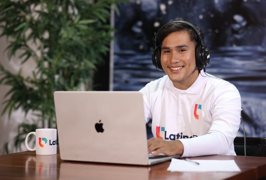 A smiling man wearing headphones works on a laptop, with a mug and pen on the table. Join our team of legal transcriptionist.