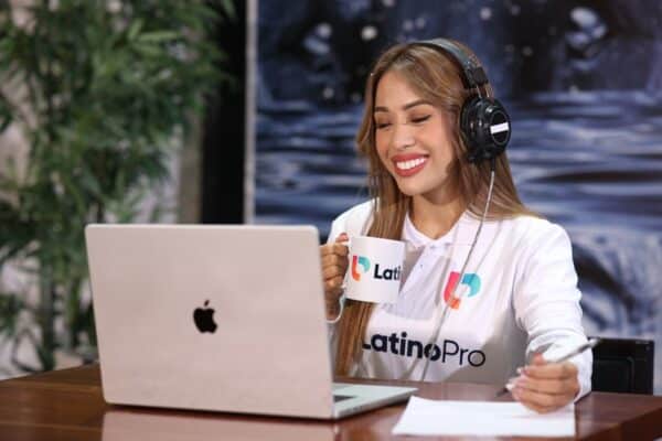 A smiling woman wearing headphones works on a laptop, holding a branded mug and pen. Learn how do i become a legal transcriptionist and start your journey today