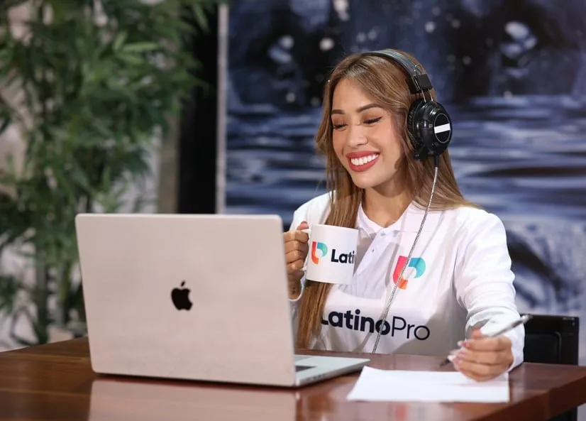 A smiling woman wearing headphones works on a laptop, holding a branded mug and pen. Learn how do i become a legal transcriptionist and start your journey today