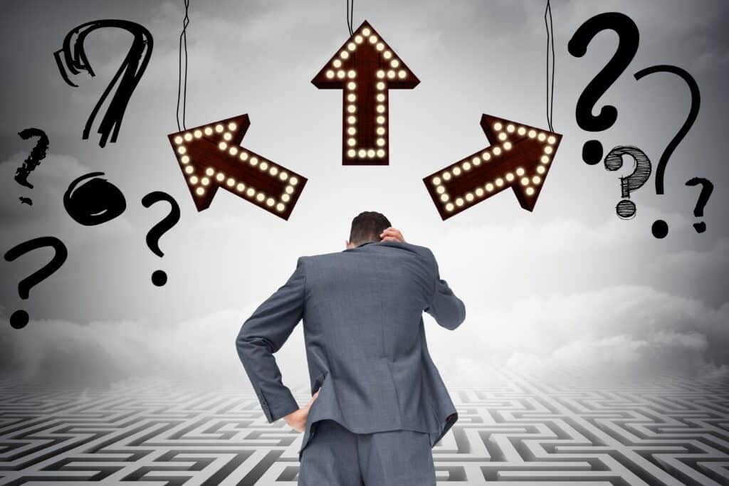 Businessman confused at crossroads with arrows and question marks, symbolizing executive administrator vs executive assistant.