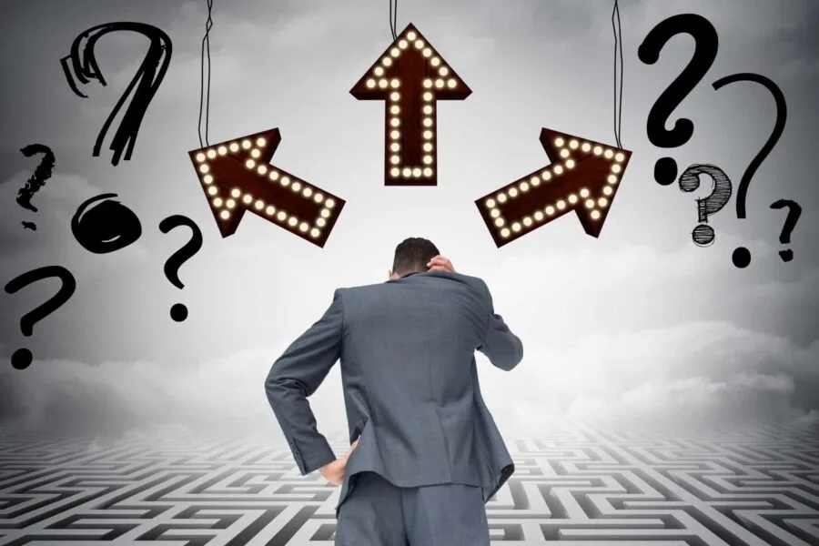 Businessman confused at crossroads with arrows and question marks, symbolizing executive administrator vs executive assistant.
