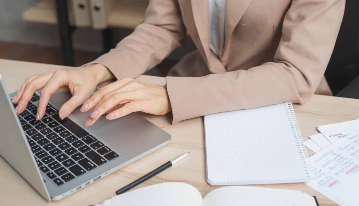 Professional typing on laptop with notes and planner, applying administrative assistant hard skills in office tasks.
