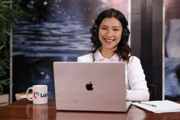 Smiling woman learning how to become a legal assistant online with laptop, headset, and study materials.