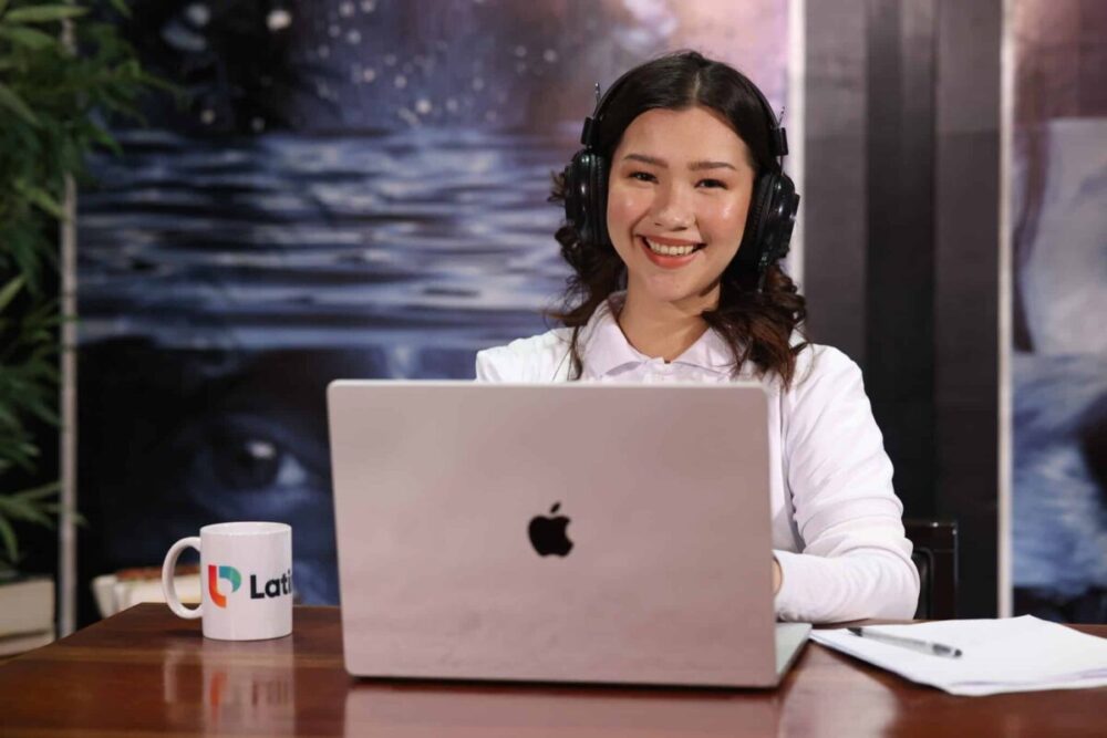 Smiling woman learning how to become a legal assistant online with laptop, headset, and study materials.
