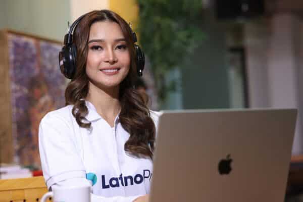 A smiling young woman with headphones sits in front of a laptop